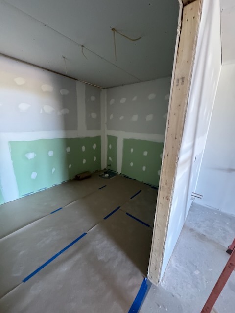 Bay 1 bathroom with drywall hung and moisture-resistant board at the lower wall, floor protection down