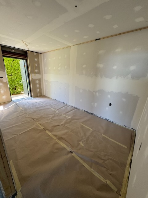 Bay 1 office with drywall taped and mudded, looking out through the personnel door